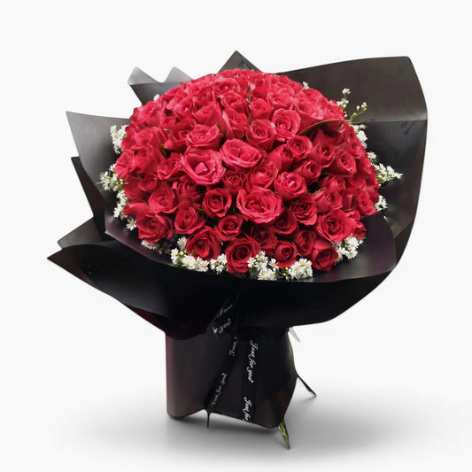 The Flowercart Meadow Fresh bouquet featuring 100 crimson roses and baby's breath wrapped in elegant black paper.