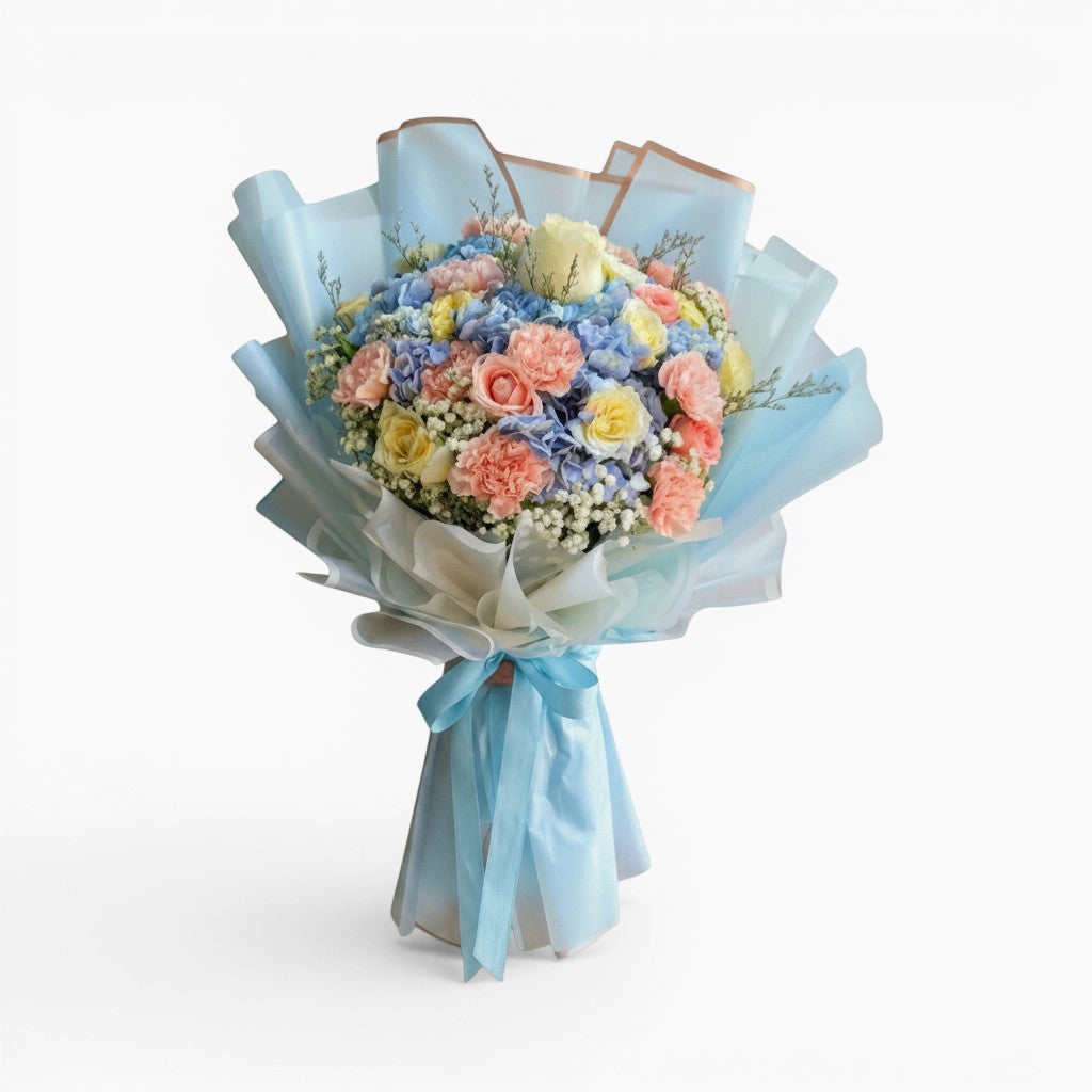 The Flowercart Pastel Blossom bouquet with pink carnations, roses, blue hydrangea, and baby's breath in blue wrapping.