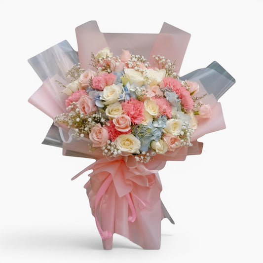The Flowercart Pastel Dreams bouquet featuring pink and white roses, carnations, blue hydrangea, and baby's breath.