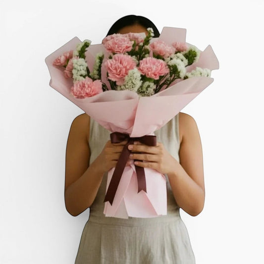 The Flowercart Divine Radiance bouquet of pink carnations and white statice wrapped in pastel pink paper.
