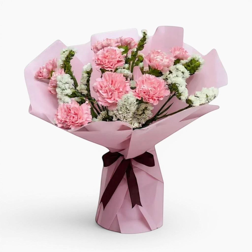 The Flowercart Divine Radiance bouquet featuring light pink carnations and white statice in pastel pink wrapping.