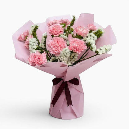The Flowercart Divine Radiance bouquet featuring light pink carnations and white statice in pastel pink wrapping.