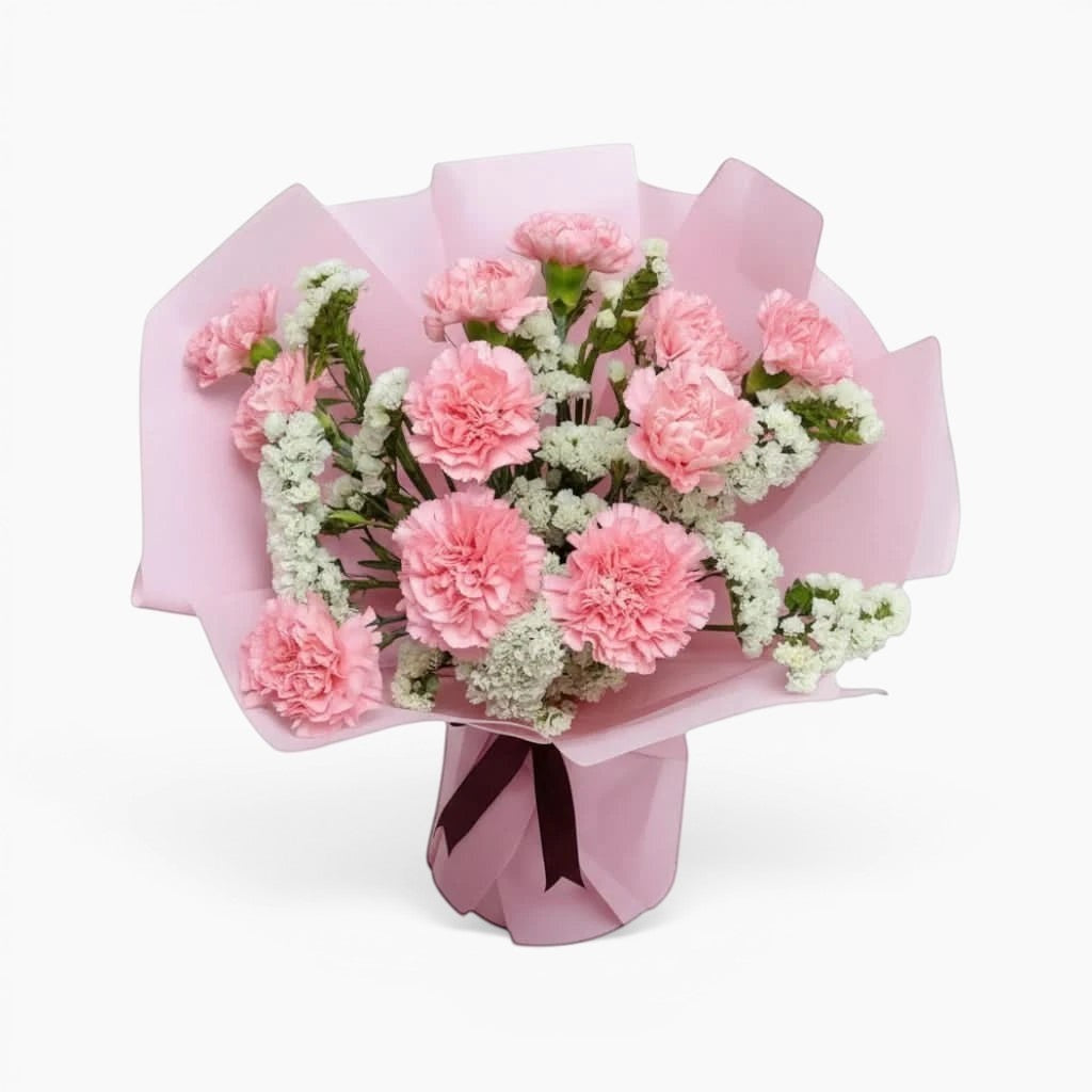 The Flowercart Divine Radiance bouquet featuring light pink carnations and white statice in pastel pink wrapping.
