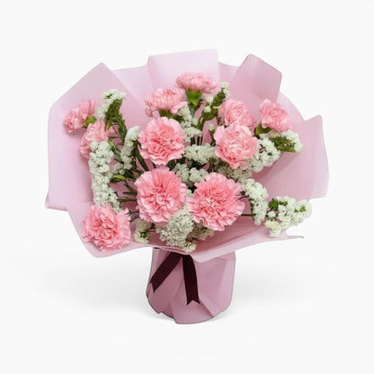 The Flowercart Divine Radiance bouquet featuring light pink carnations and white statice in pastel pink wrapping.
