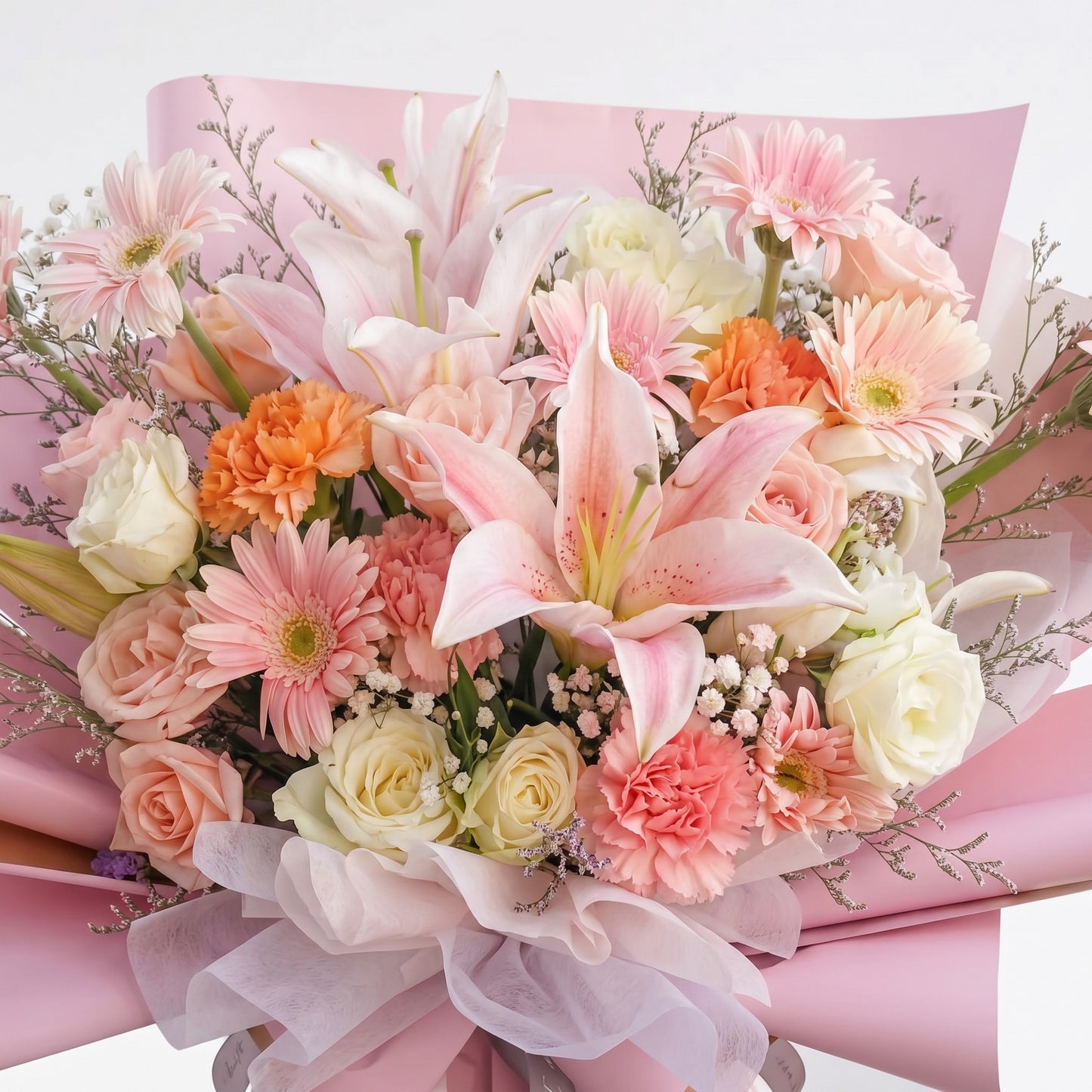 The Flowercart Enchanté Bloom bouquet featuring pink lilies, roses, gerberas, and carnations in pink wrapping paper.