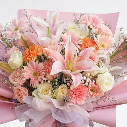 The Flowercart Enchanté Bloom bouquet featuring pink lilies, roses, gerberas, and carnations in pink wrapping paper.