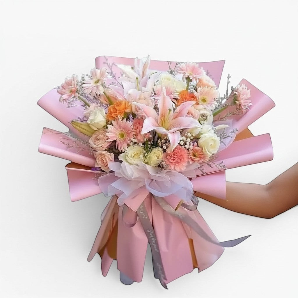 The Flowercart Enchanté Bloom bouquet with pink lilies, roses, carnations, and gerberas wrapped in pink paper.