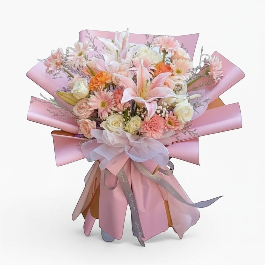 The Flowercart Enchanté Bloom bouquet with pink lilies, roses, gerberas, and carnations wrapped in pink paper.