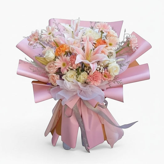 The Flowercart Enchanté Bloom bouquet with pink lilies, roses, gerberas, and carnations wrapped in pink paper.