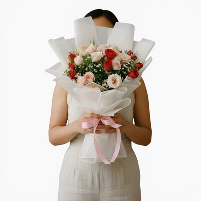The Flowercart Blushing Harmony bouquet of 24 pink and red roses wrapped in white paper with a soft pink ribbon.