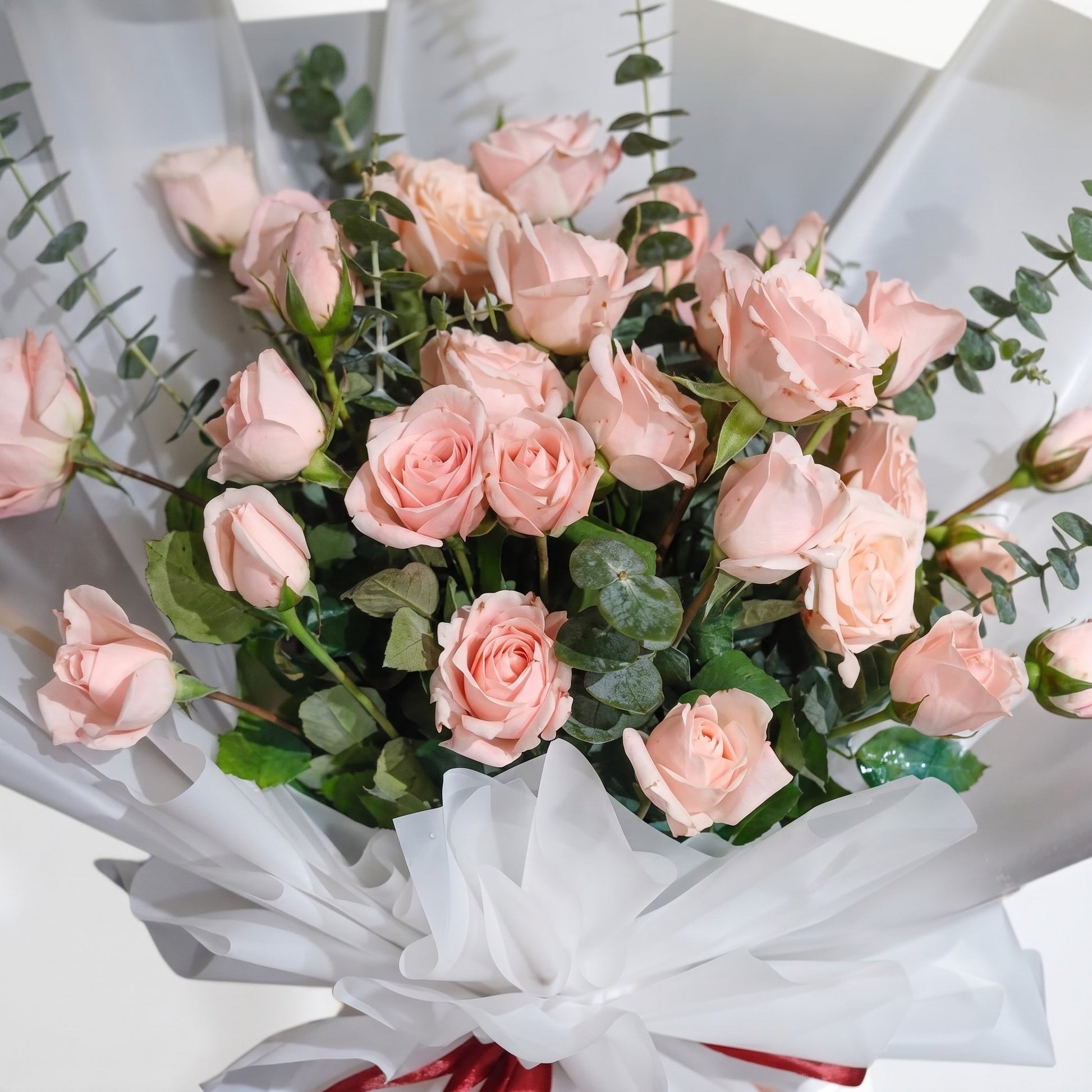 The Flowercart Lovely Spark bouquet featuring 24 baby pink roses and fresh eucalyptus wrapped in white paper.