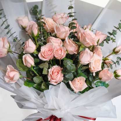 The Flowercart Lovely Spark bouquet featuring 24 baby pink roses and fresh eucalyptus wrapped in white paper.