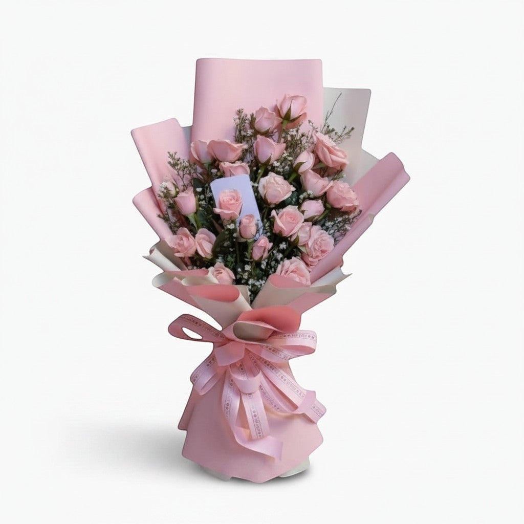 The Flowercart Pink Whisper bouquet featuring 24 fresh pink roses and baby's breath wrapped in elegant pink paper.
