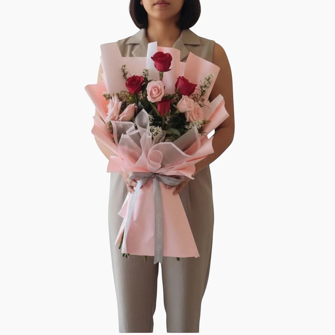 The Flowercart Caribbean Twist bouquet featuring red and pink roses wrapped in elegant pink paper held by a person.