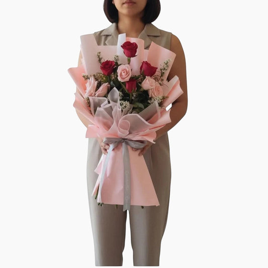 The Flowercart Caribbean Twist bouquet featuring red and pink roses wrapped in elegant pink paper held by a person.