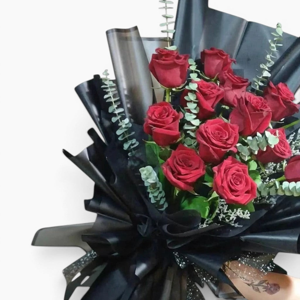 The Flowercart Maison Fleur bouquet featuring 12 red Ecuadorian roses and fresh eucalyptus wrapped in black paper.