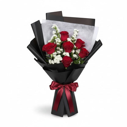 The Flowercart Hot Romance bouquet featuring six red roses and white statice wrapped in elegant black paper with a bow.