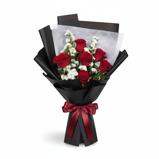 The Flowercart Hot Romance bouquet featuring six red roses and white statice wrapped in elegant black paper with a bow.