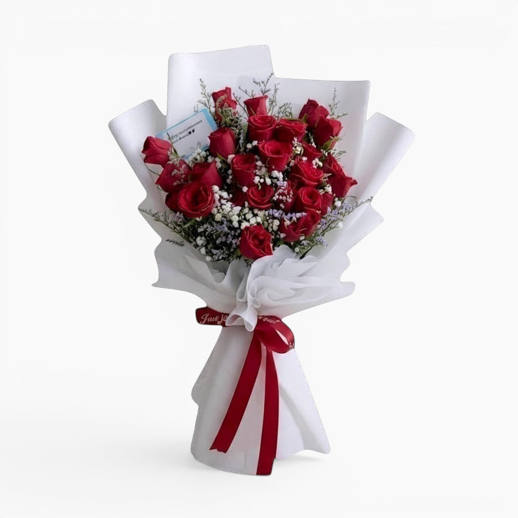 The Flowercart Fallin For You bouquet featuring 24 deep red roses with baby's breath in white paper wrapping.