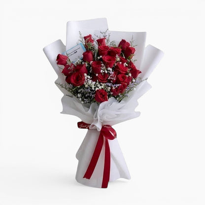 The Flowercart Fallin For You bouquet featuring 24 deep red roses with baby's breath in white paper wrapping.