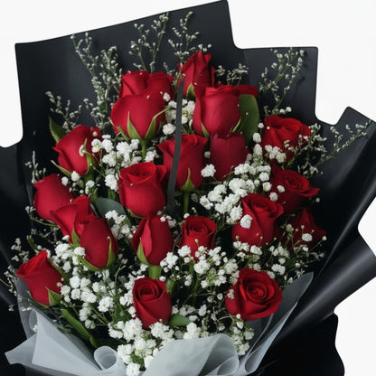The Flowercart Luxe Noir bouquet of 24 red roses with white fillers wrapped in elegant black paper and red ribbon.