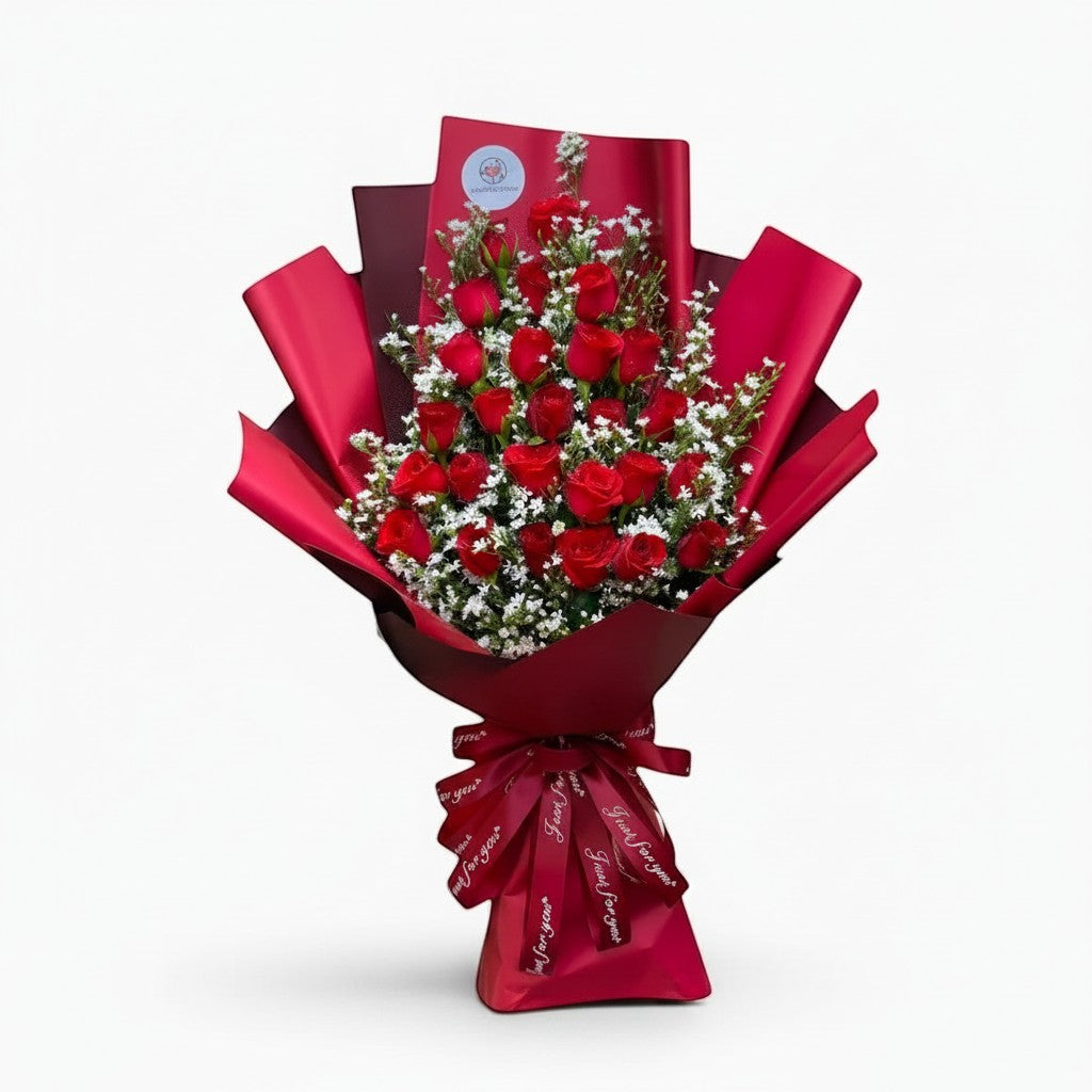 The Flowercart Valley Scent bouquet of 24 red roses and baby's breath wrapped in red paper with a decorative ribbon.
