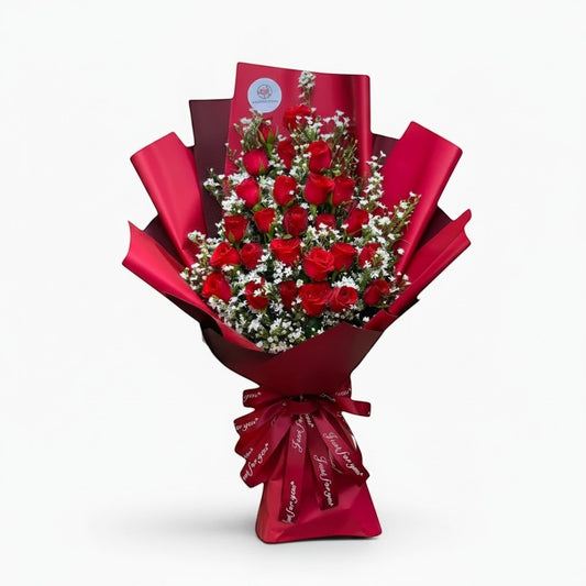 The Flowercart Valley Scent bouquet of 24 red roses and baby's breath wrapped in red paper with a decorative ribbon.
