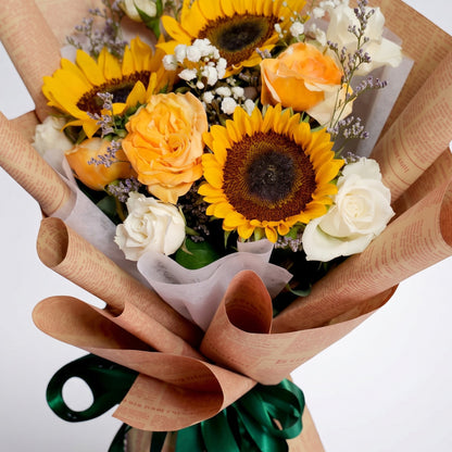 The Flowercart Sunny Serenade bouquet with sunflowers, yellow and white roses, and baby's breath in rustic paper.