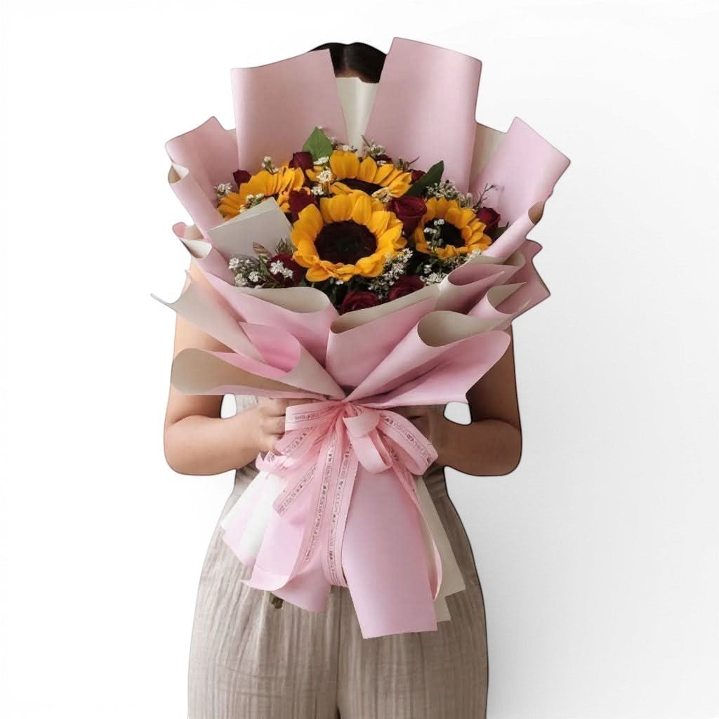 The Flowercart sunflower and red rose bouquet wrapped in pink paper, held by a person for a romantic gift.