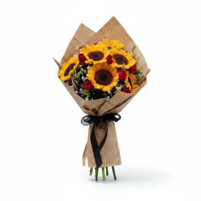 The Flowercart Sunny Blooms bouquet featuring sunflowers, red roses, and baby's breath wrapped in vintage newspaper.