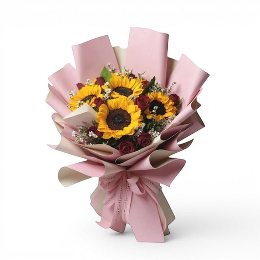 The Flowercart Velvet Magnolia bouquet featuring yellow sunflowers and red roses wrapped in elegant pink paper.