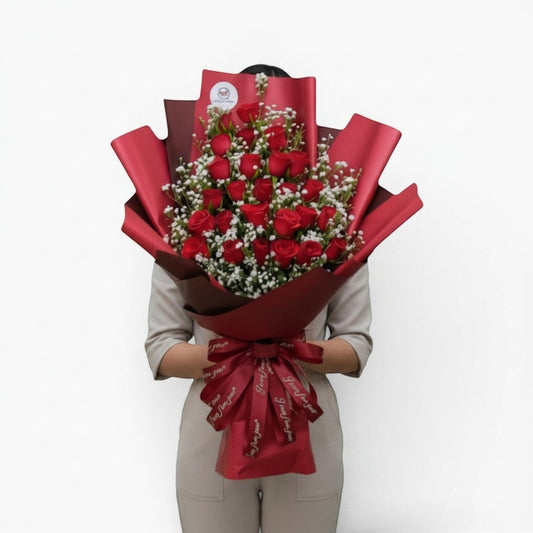 The Flowercart Valley Scent bouquet of 24 red roses and baby's breath wrapped in red paper with a decorative ribbon.