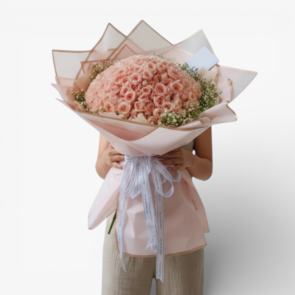 The Flowercart 199 baby pink roses bouquet with baby's breath, wrapped in pink paper and tied with a white ribbon.