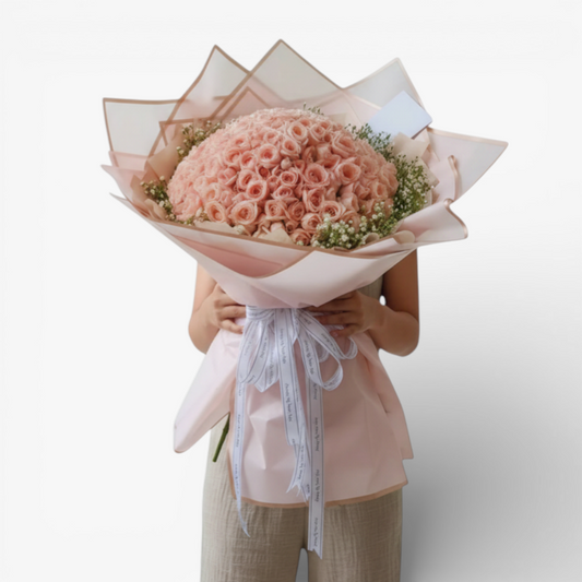 The Flowercart 199 baby pink roses bouquet with baby's breath, wrapped in pink paper and tied with a white ribbon.