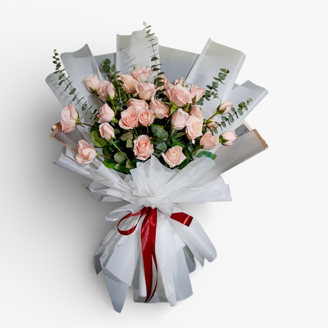 The Flowercart Lovely Spark bouquet: 24 baby pink roses with eucalyptus, wrapped in white paper and tied with a red ribbon.