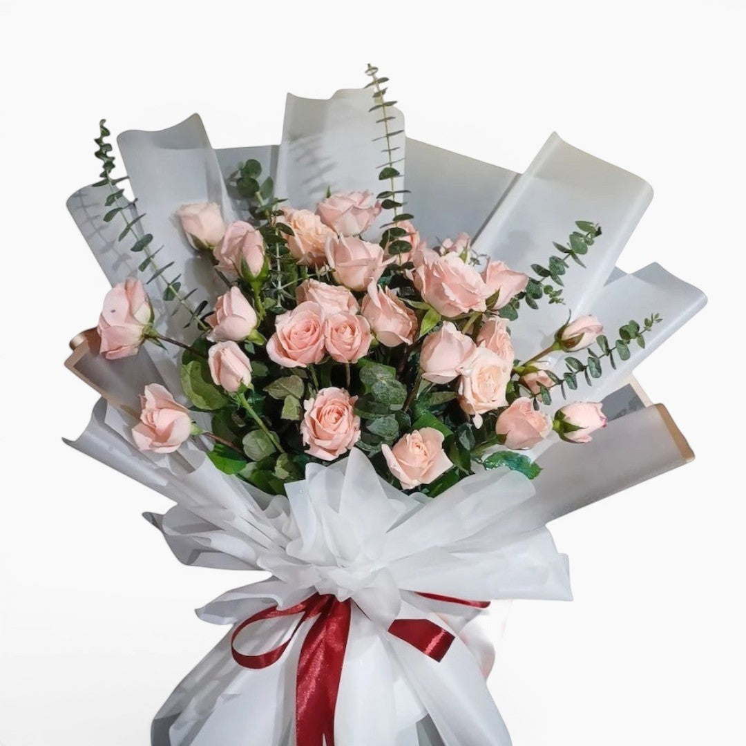 The Flowercart Lovely Spark bouquet with 24 baby pink roses and eucalyptus, wrapped in white paper with a burgundy ribbon.