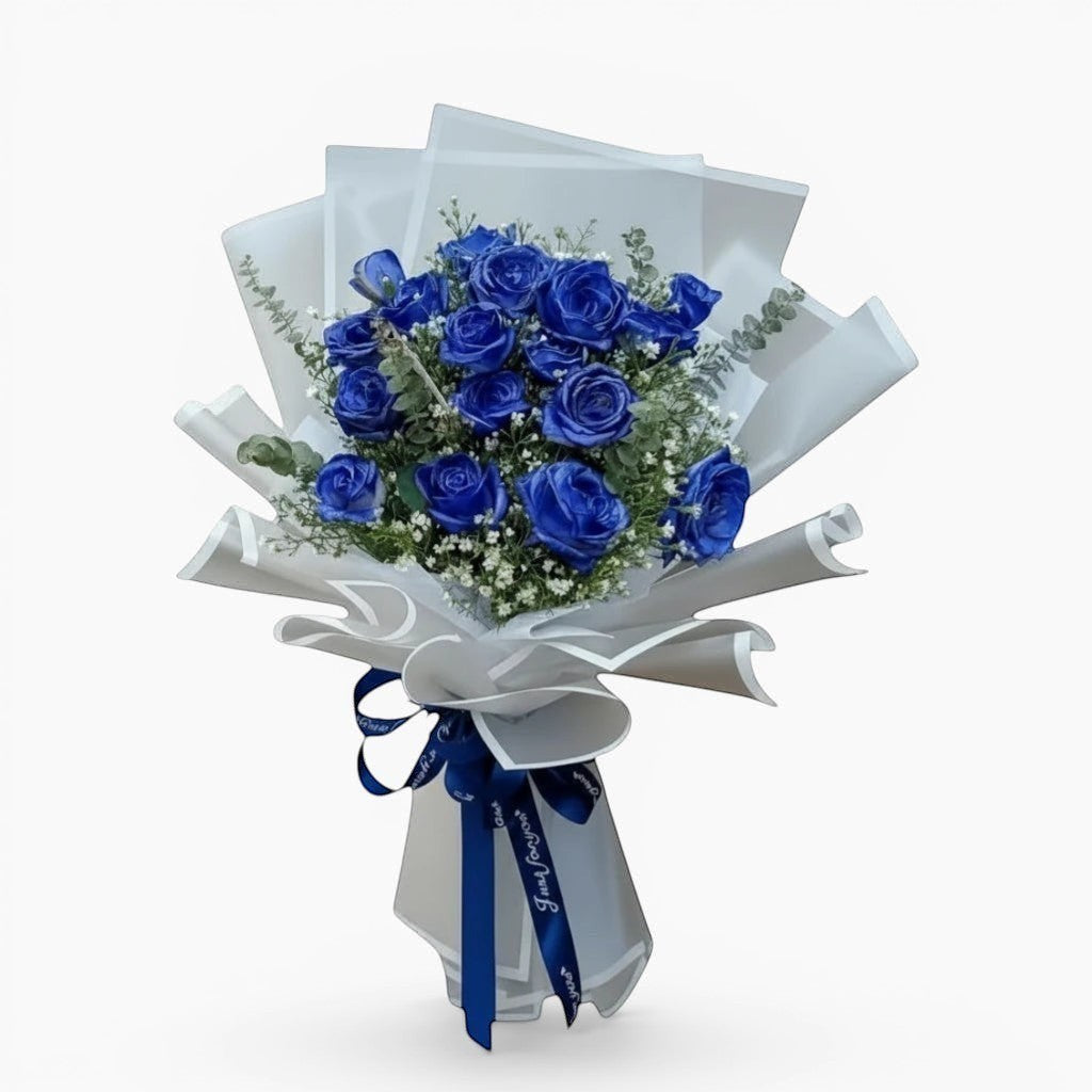 The Flowercart Sapphire Devotion Bouquet: 16 vibrant blue spray roses with baby's breath and eucalyptus, wrapped in white paper and tied with a blue ribbon.