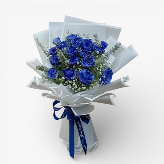 The Flowercart Sapphire Devotion Bouquet: 16 vibrant blue spray roses with baby's breath and eucalyptus, wrapped in white paper and tied with a blue ribbon.