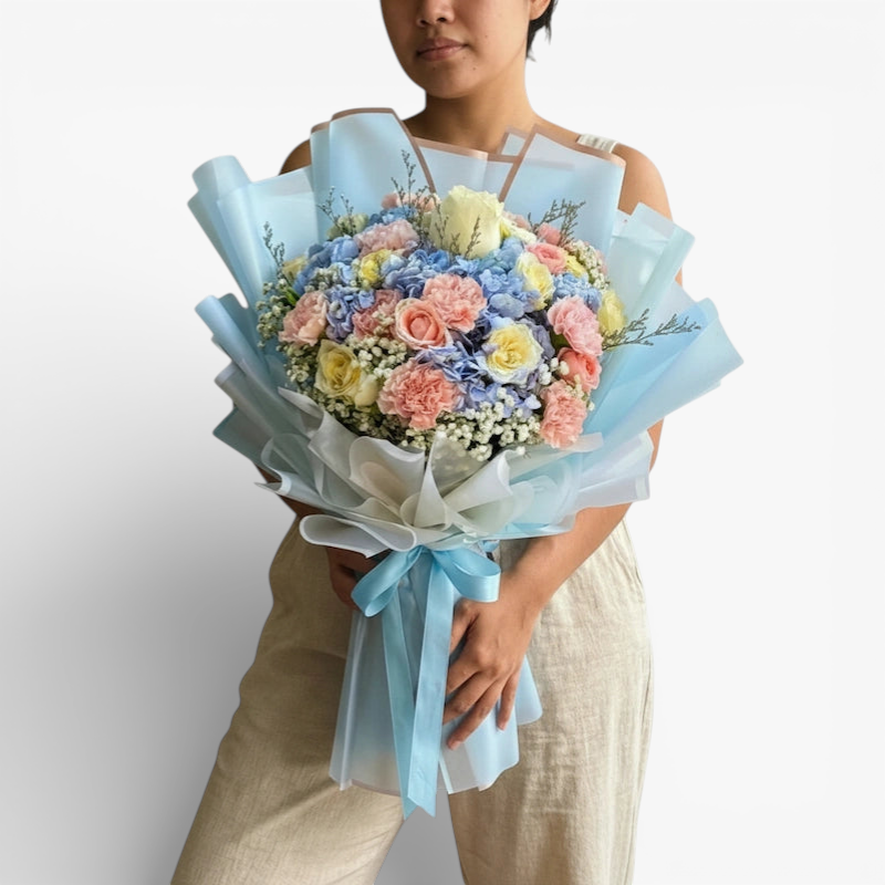 The Flowercart Pastel Blossom bouquet with pink roses, white roses, blue hydrangea, pink carnations, and baby's breath.