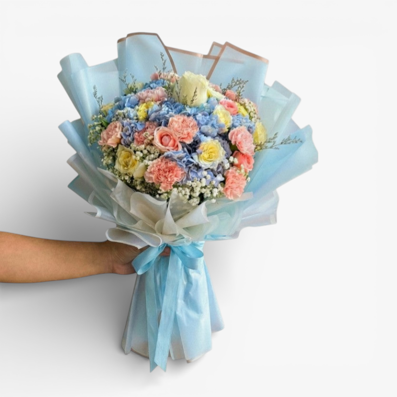The Flowercart Pastel Blossom bouquet with pink roses, white roses, blue hydrangea, yellow roses, pink carnations, and baby's breath.