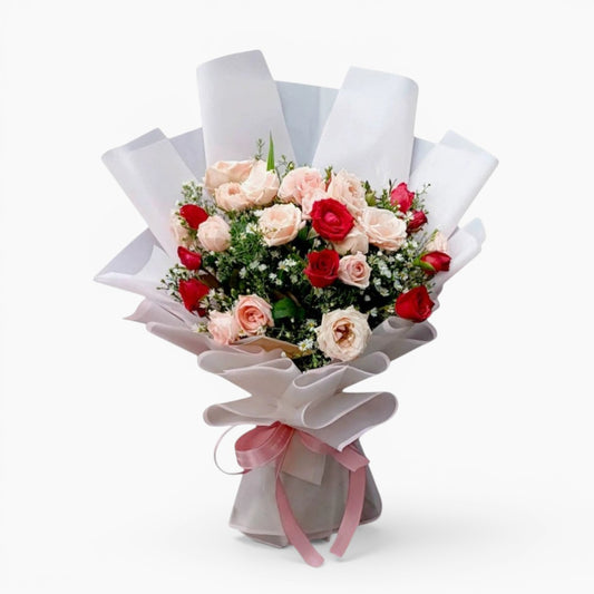 The Flowercart Blushing Harmony bouquet with 24 pink and red roses, elegantly wrapped in white paper with a pink ribbon.