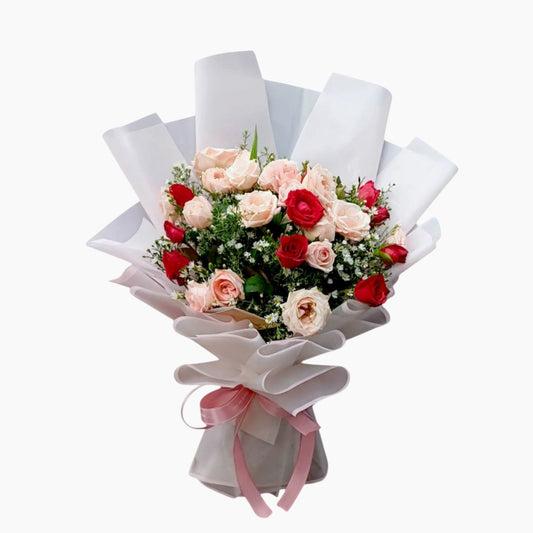 The Flowercart Blushing Harmony bouquet with 24 pink and red roses, elegantly wrapped in white paper with a pink ribbon.