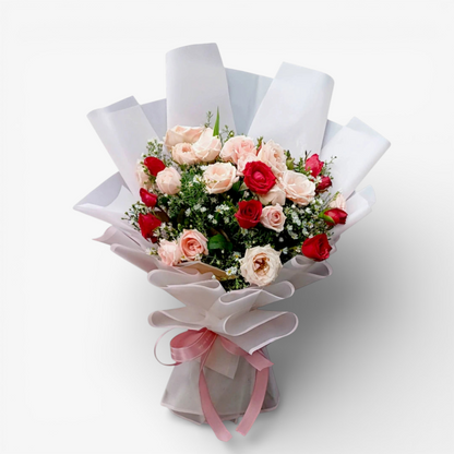 The Flowercart Blushing Harmony bouquet with 24 pink and red roses, elegantly wrapped in white paper with a pink ribbon.