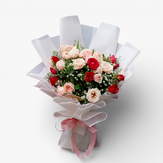 The Flowercart Blushing Harmony bouquet with 24 pink and red roses, elegantly wrapped in white paper with a pink ribbon.