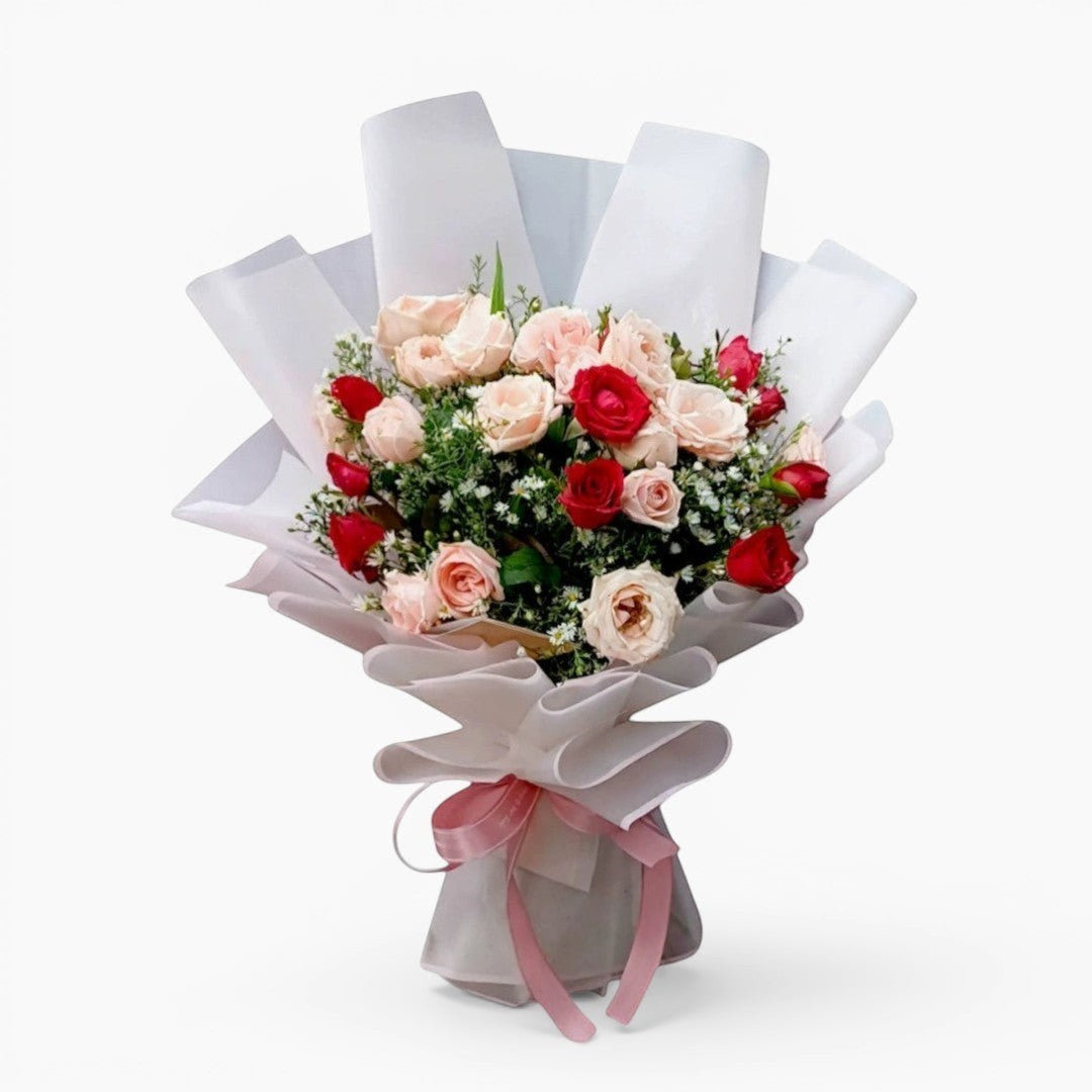 The Flowercart Blushing Harmony bouquet with 24 pink and red roses, elegantly wrapped in white paper with a pink ribbon.