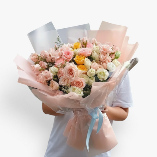 The Flowercart's Fior di Luna bouquet features pink, white, and yellow roses with baby's breath, wrapped in pink and silver paper.