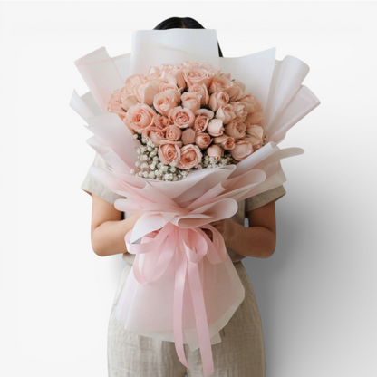 The Flowercart's Mardigrass bouquet features 50 premium pink roses with baby's breath, wrapped in white and pink paper with a pink ribbon.