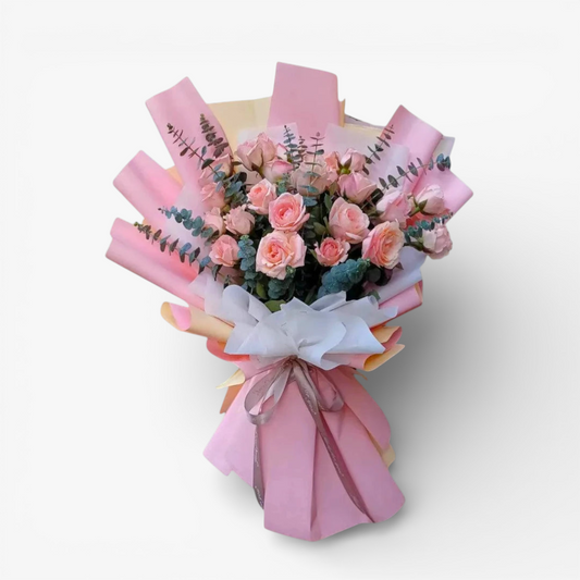 The Flowercart Serene Pink Rose bouquet features 24 soft pink roses and eucalyptus, wrapped in blush paper with a ribbon.