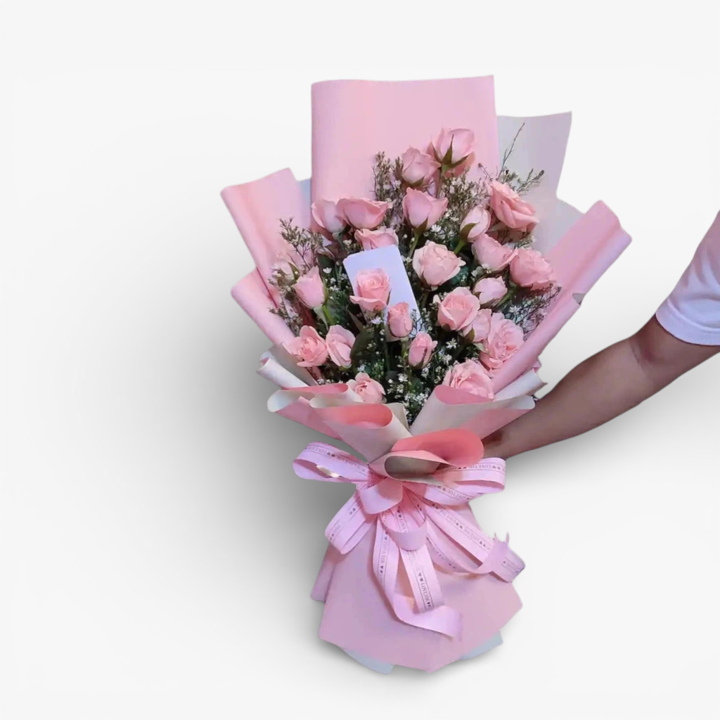 The Flowercart Pink Whisper bouquet features 24 premium pink roses and baby's breath, elegantly wrapped in pink paper with a matching ribbon. Ideal for romantic occasions.
