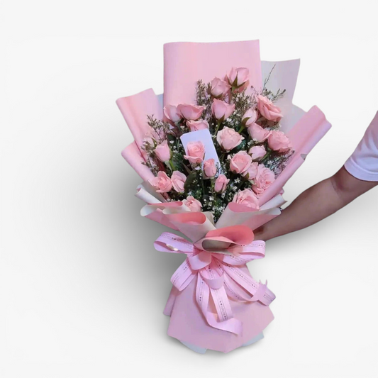 The Flowercart Pink Whisper bouquet features 24 premium pink roses and baby's breath, elegantly wrapped in pink paper with a matching ribbon. Ideal for romantic occasions.